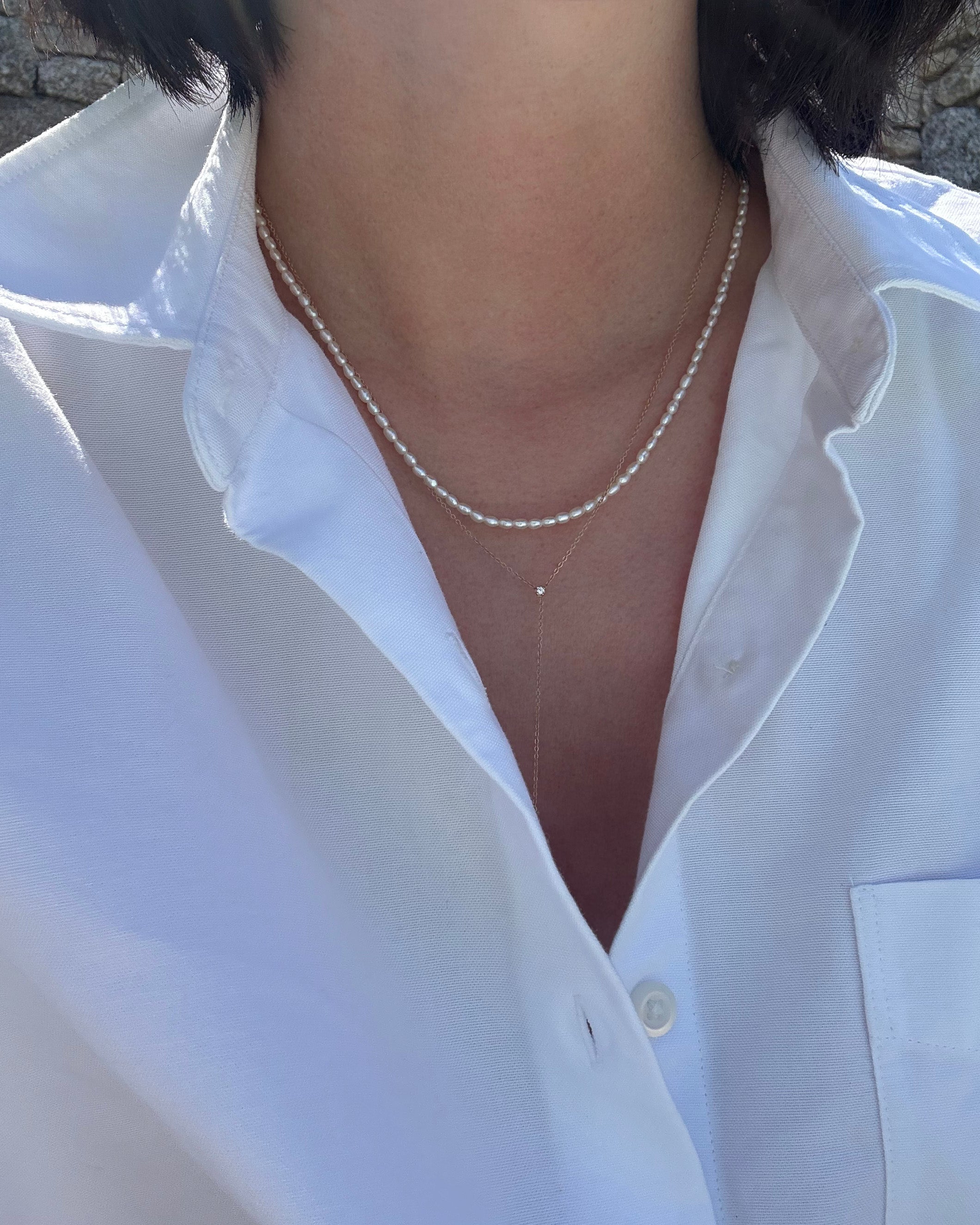 Person wearing a white shirt with a pearl necklace