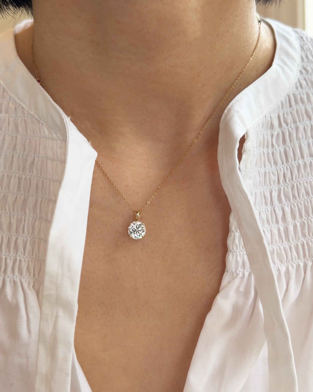Gold necklace with a diamond pendant worn by a person in a white blouse.