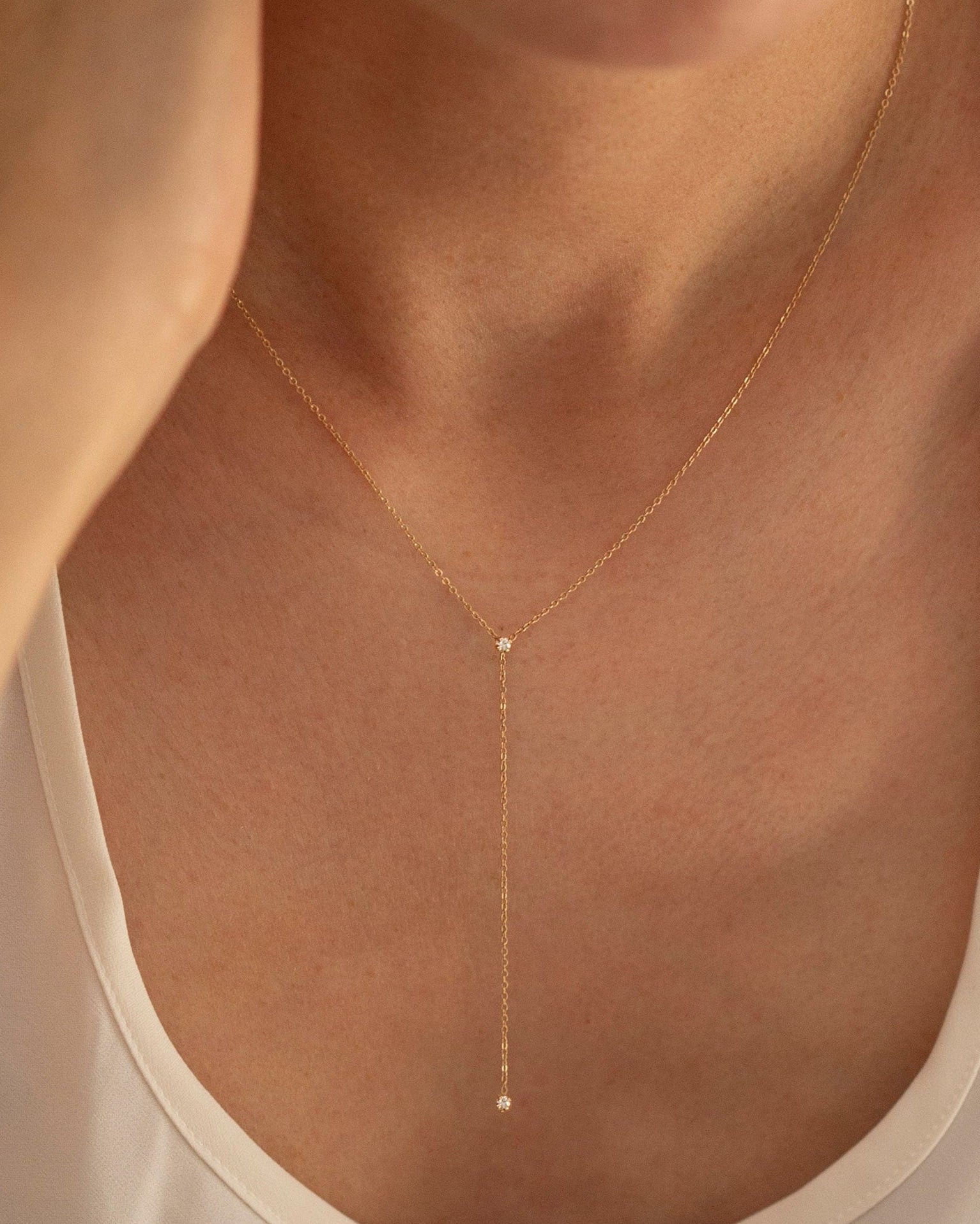 Gold necklace with a small pendant worn by a person in a white top.