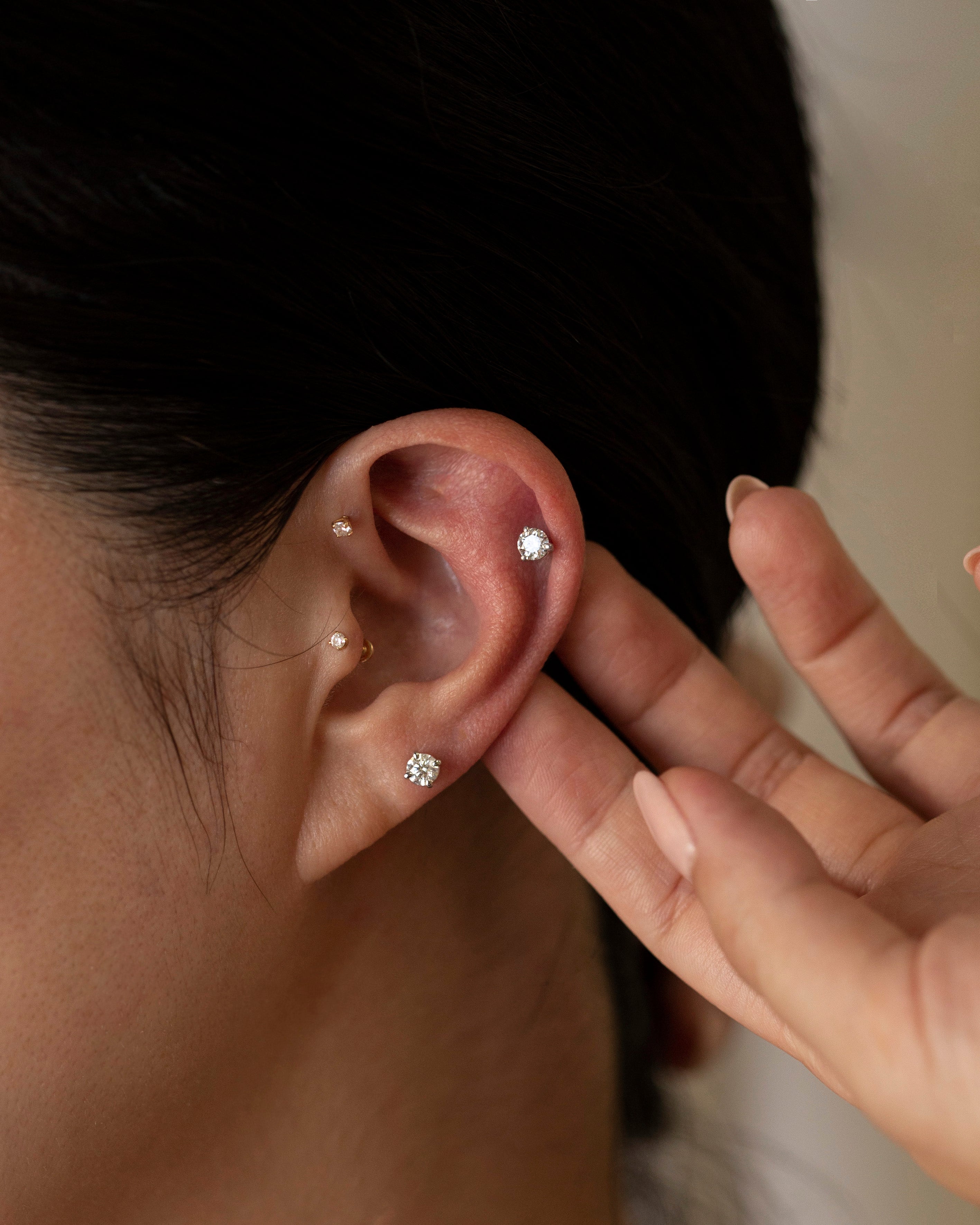 Close-up of an ear with diamond earrings and a hand touching the earlobe.