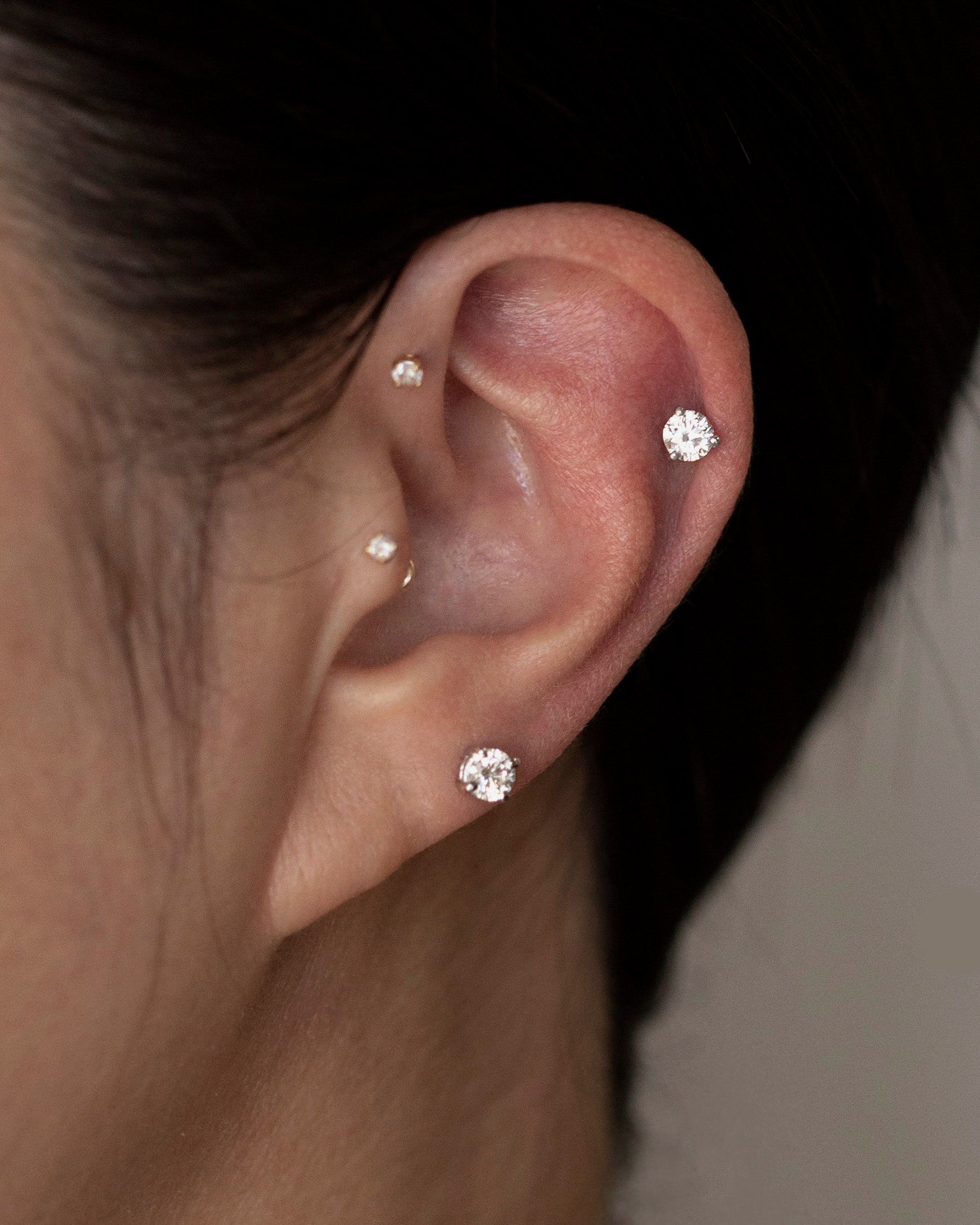 Close-up of an ear wearing three diamond stud earrings with a blurred background.