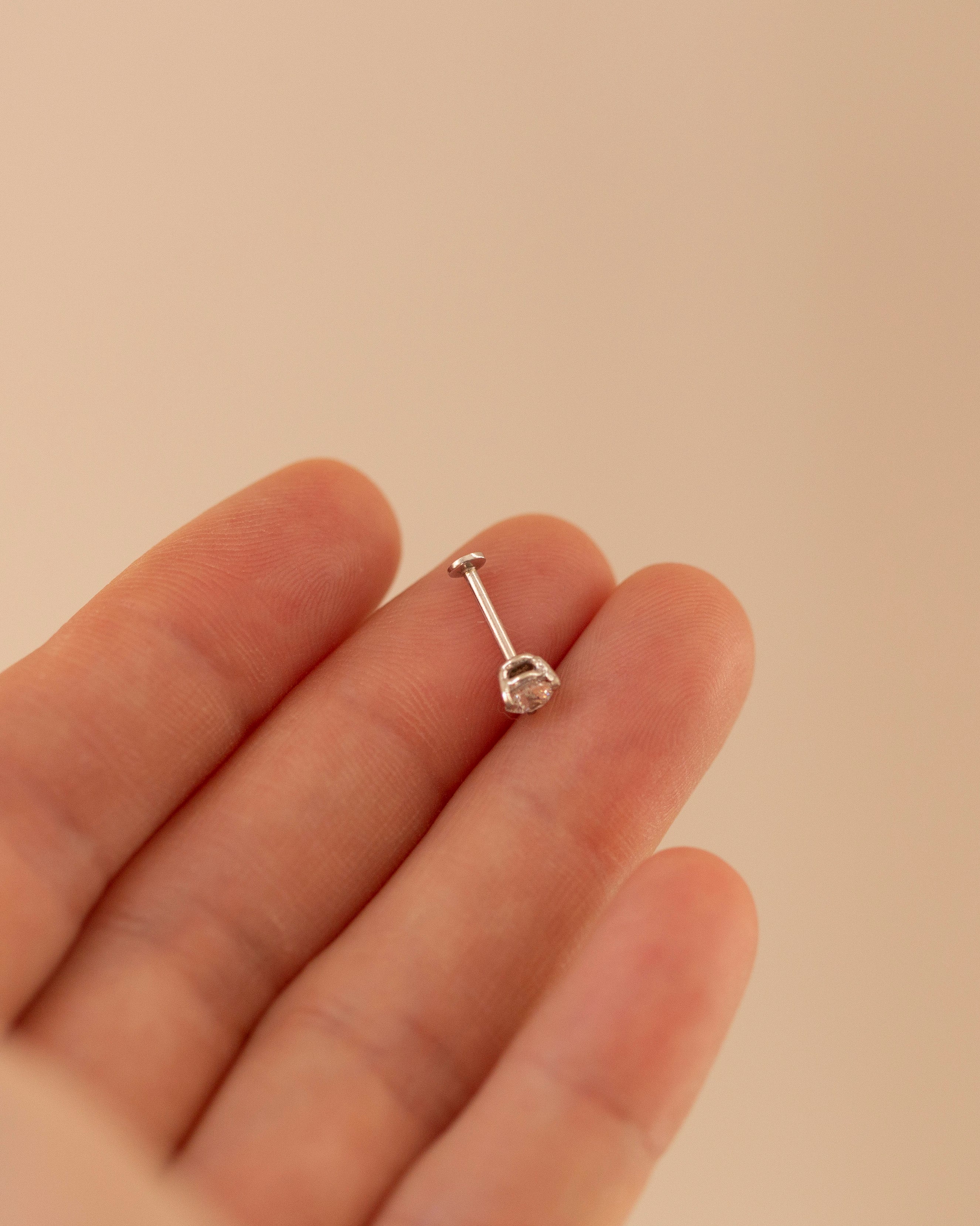 Silver barbell earring on a hand against a beige background