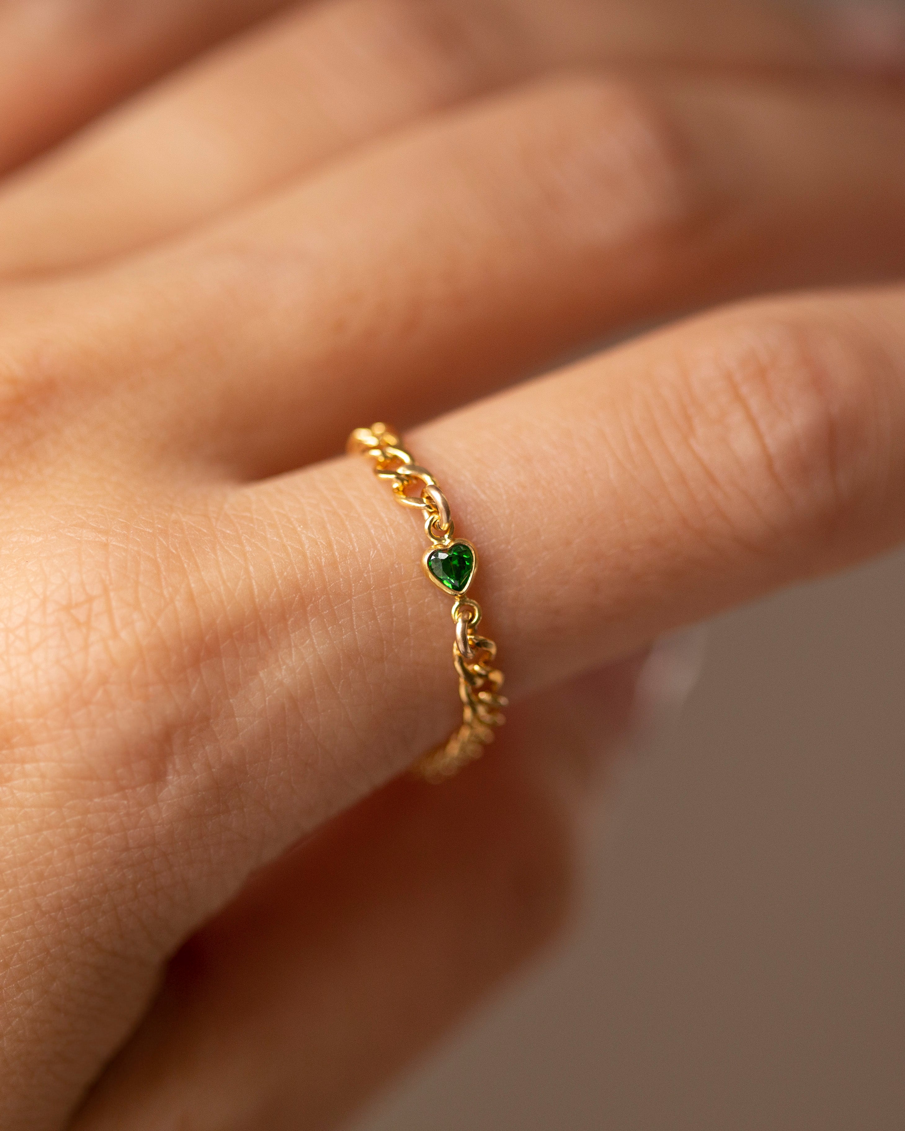 Gold ring with a green gemstone on a person's finger against a neutral background