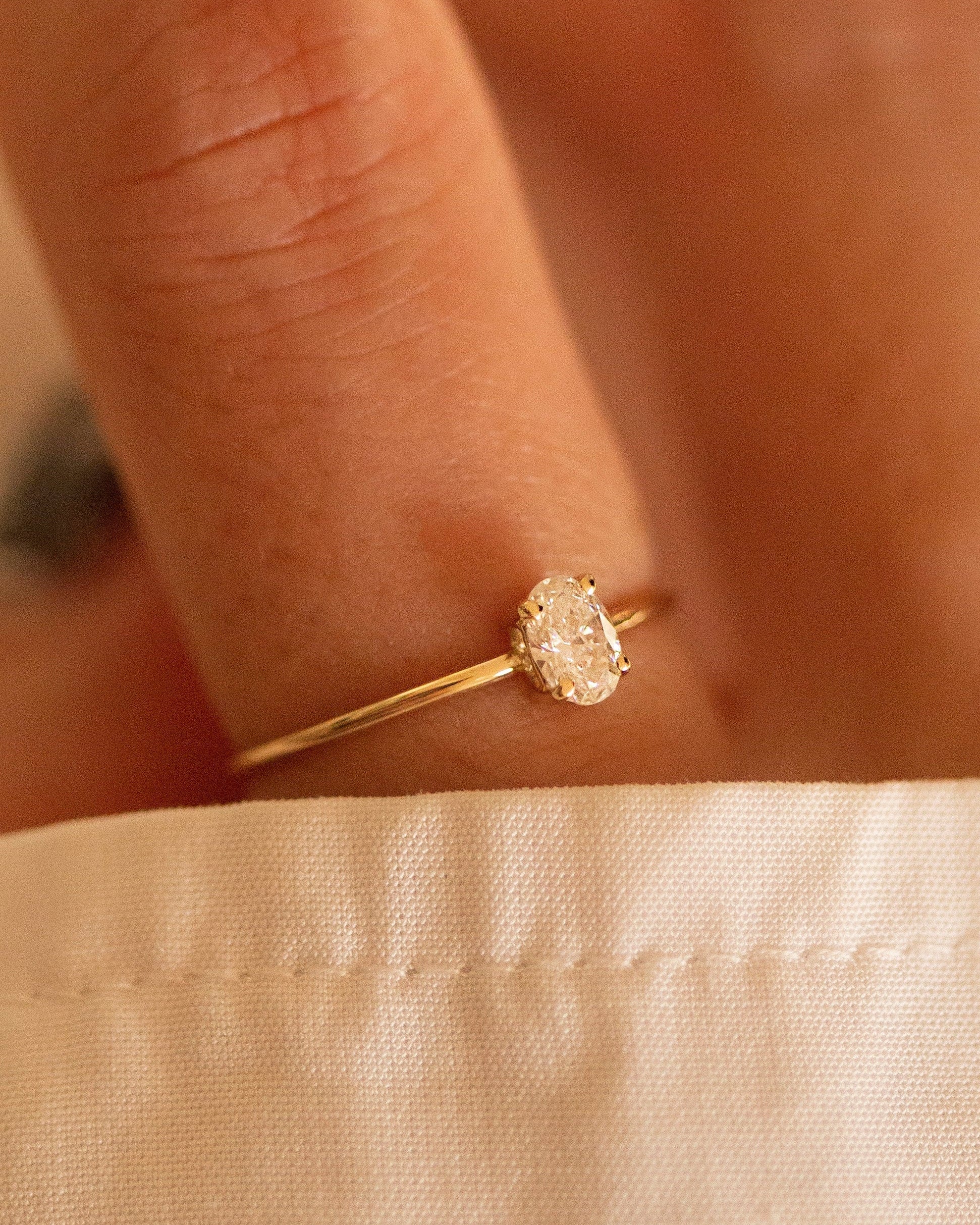 Gold ring with a diamond on a person's finger against a beige fabric background