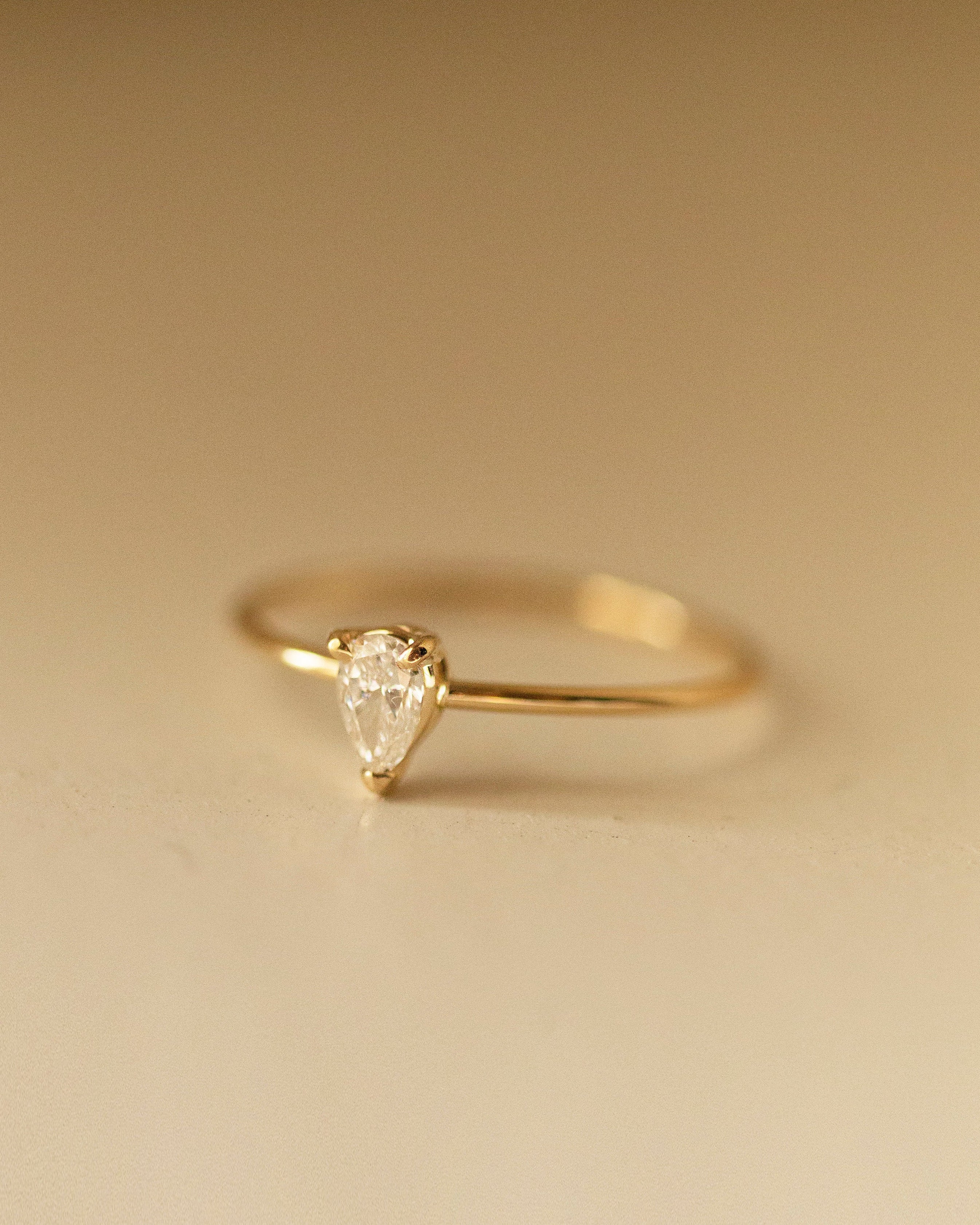 Gold ring with a pear-shaped diamond on a beige background