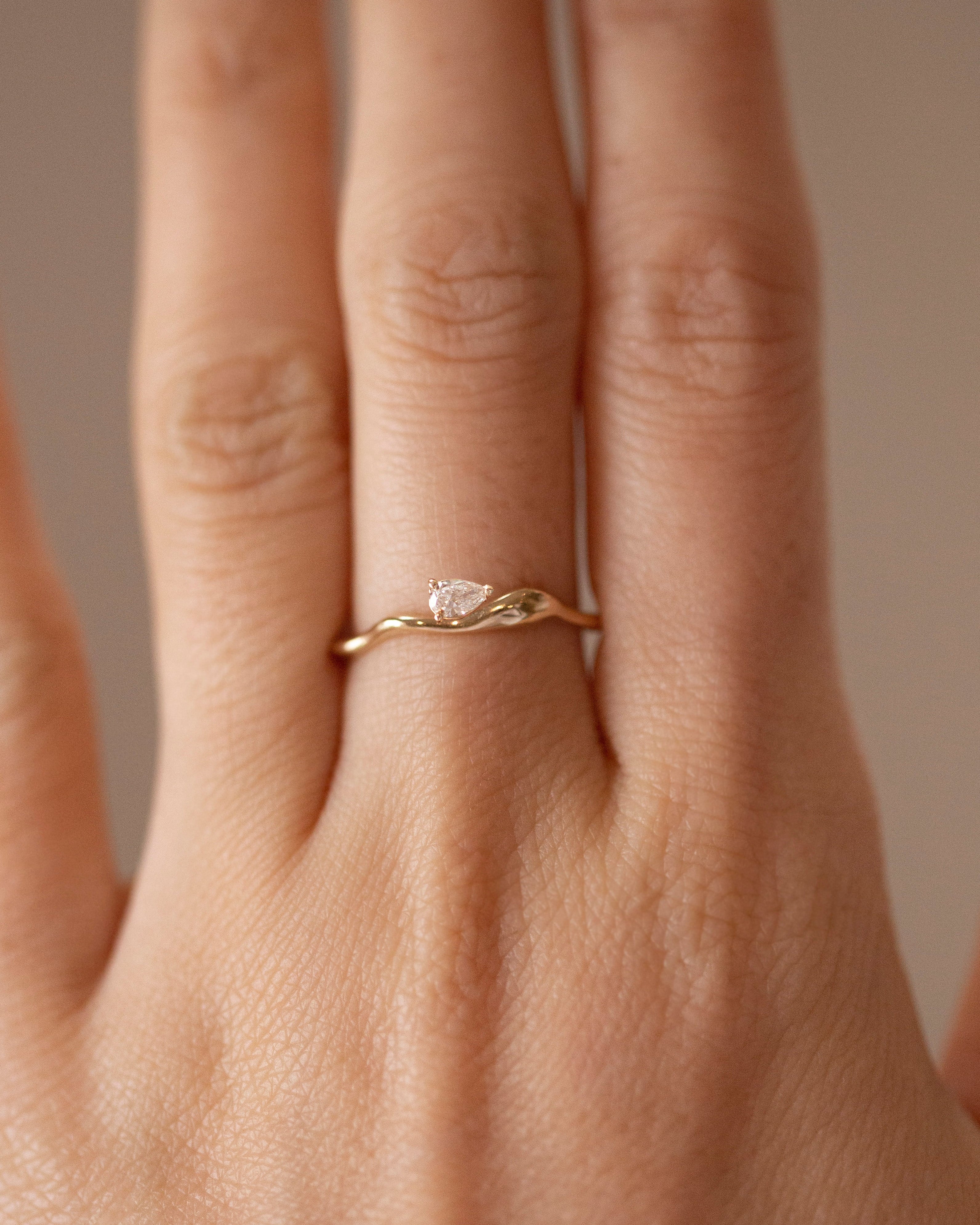 Gold ring with a diamond on a person's finger against a neutral background