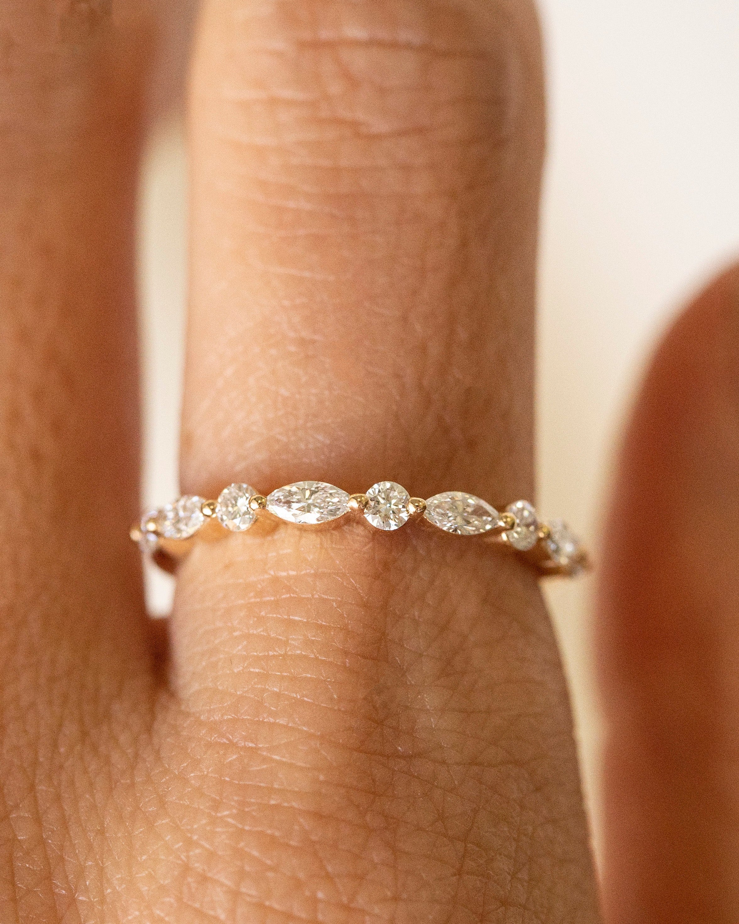 A close-up of a delicate gold ring with a row of small marquise-cut and round clear gemstones worn on a finger.