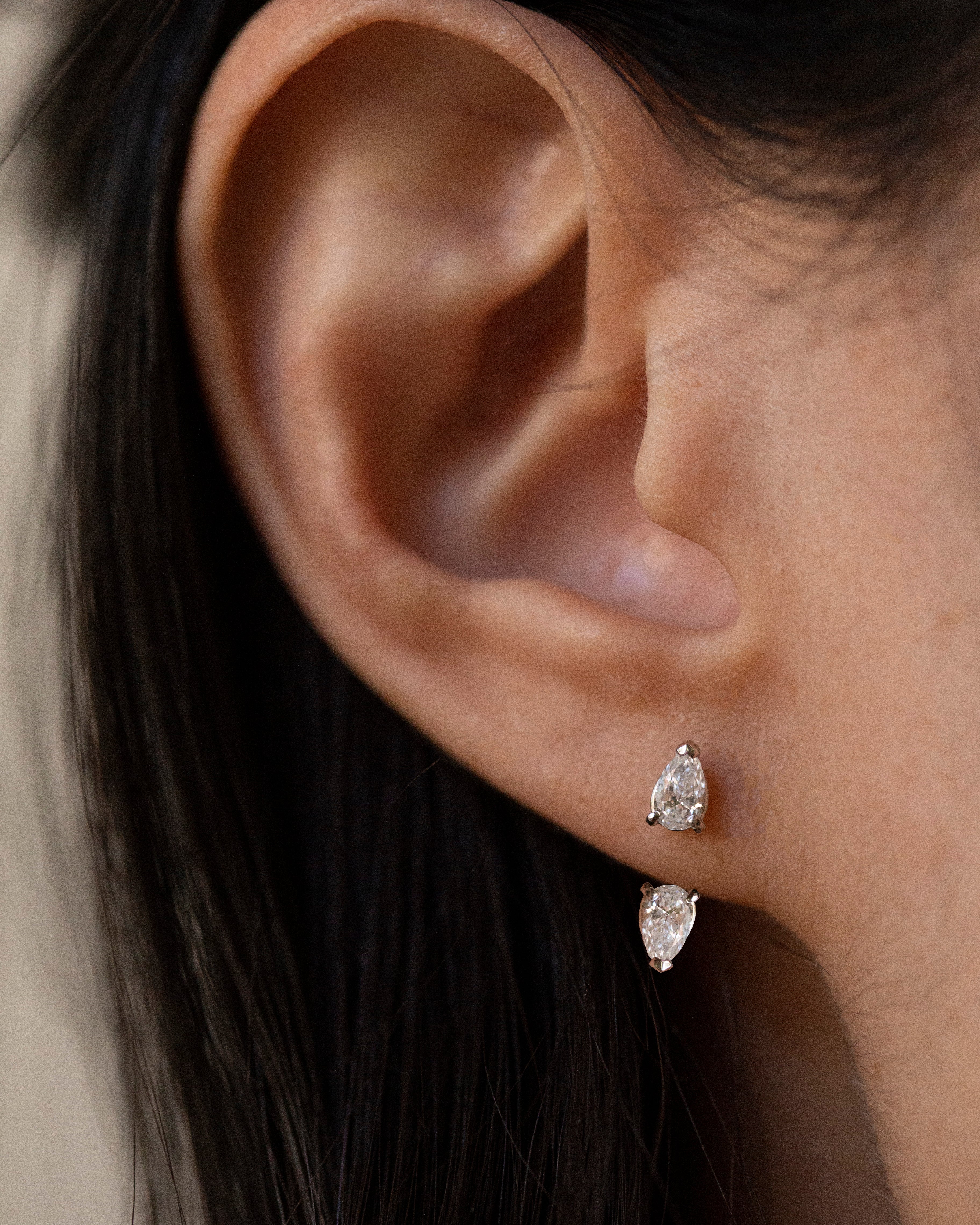 Close-up of a person's ear wearing a pair of silver-tone drop earrings with marquise-cut clear stones.