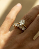 A close-up of a hand wearing a yellow gold ring set with multiple clear diamonds, including a prominent marquise-cut center stone.