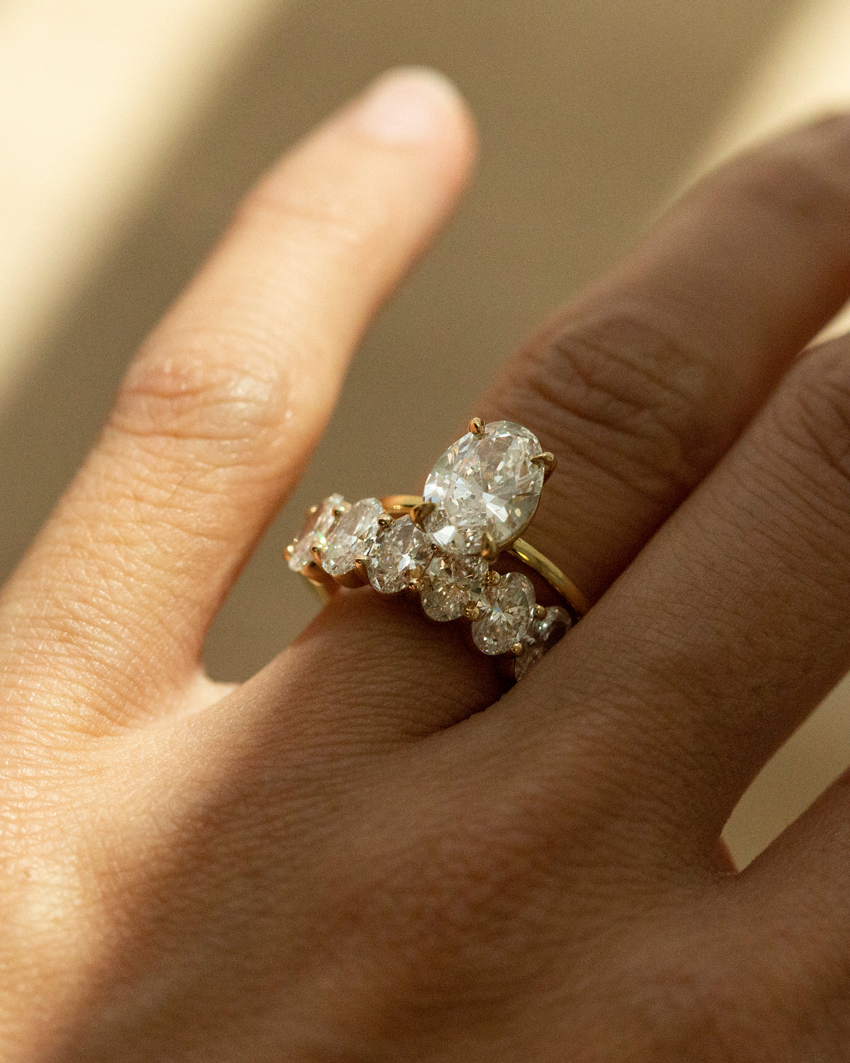 A close-up of a hand wearing a yellow gold ring set with multiple clear diamonds, including a prominent marquise-cut center stone.
