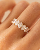 A close-up of a hand wearing a delicate gold band ring set with five round-cut clear stones.
