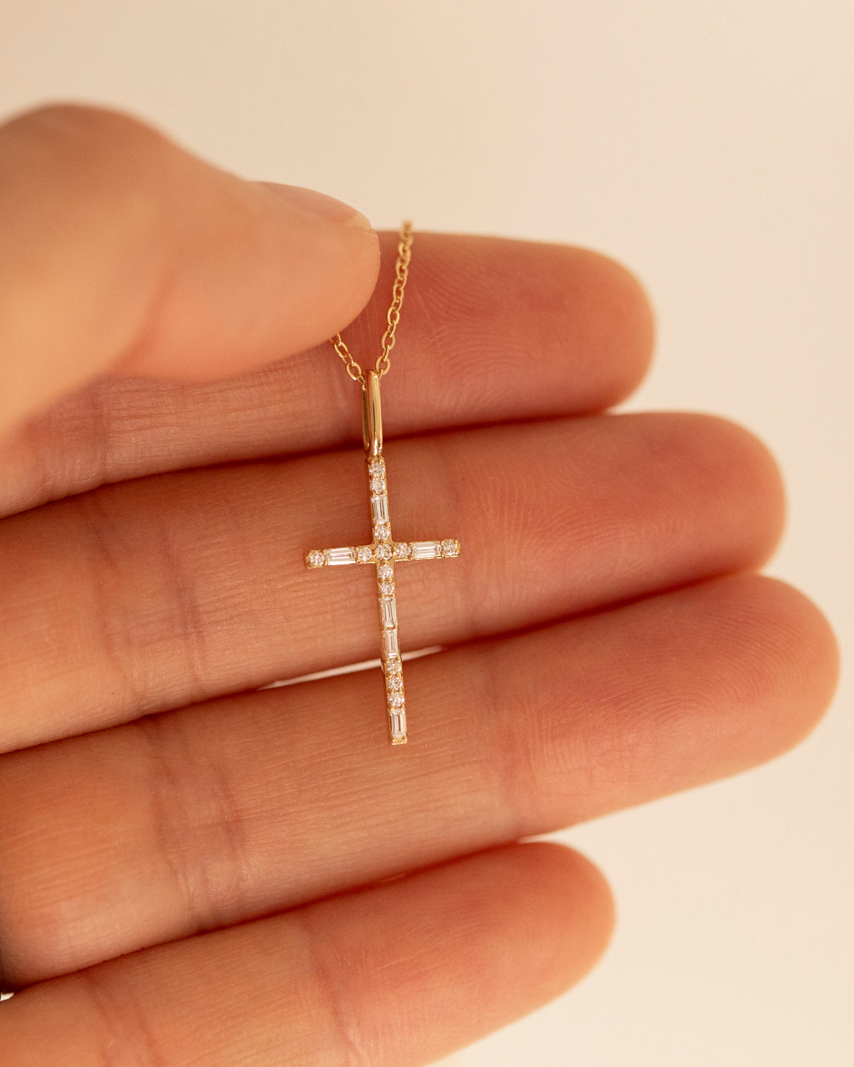 Delicate 14K yellow gold cross necklace featuring baguette and round lab-grown diamonds in an elongated cross pendant design, shown against fingers for scale.