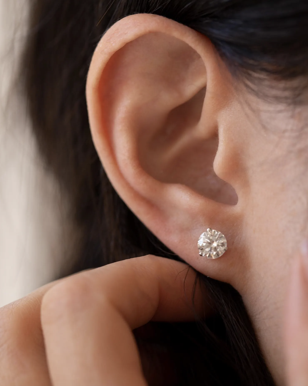 Close-up of an ear wearing a diamond stud earring with a blurred background