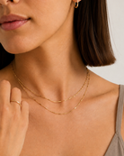 A close-up of a woman wearing a delicate double-layered gold chain necklace with a thin textured top chain and a slightly thicker smoother bottom chain.