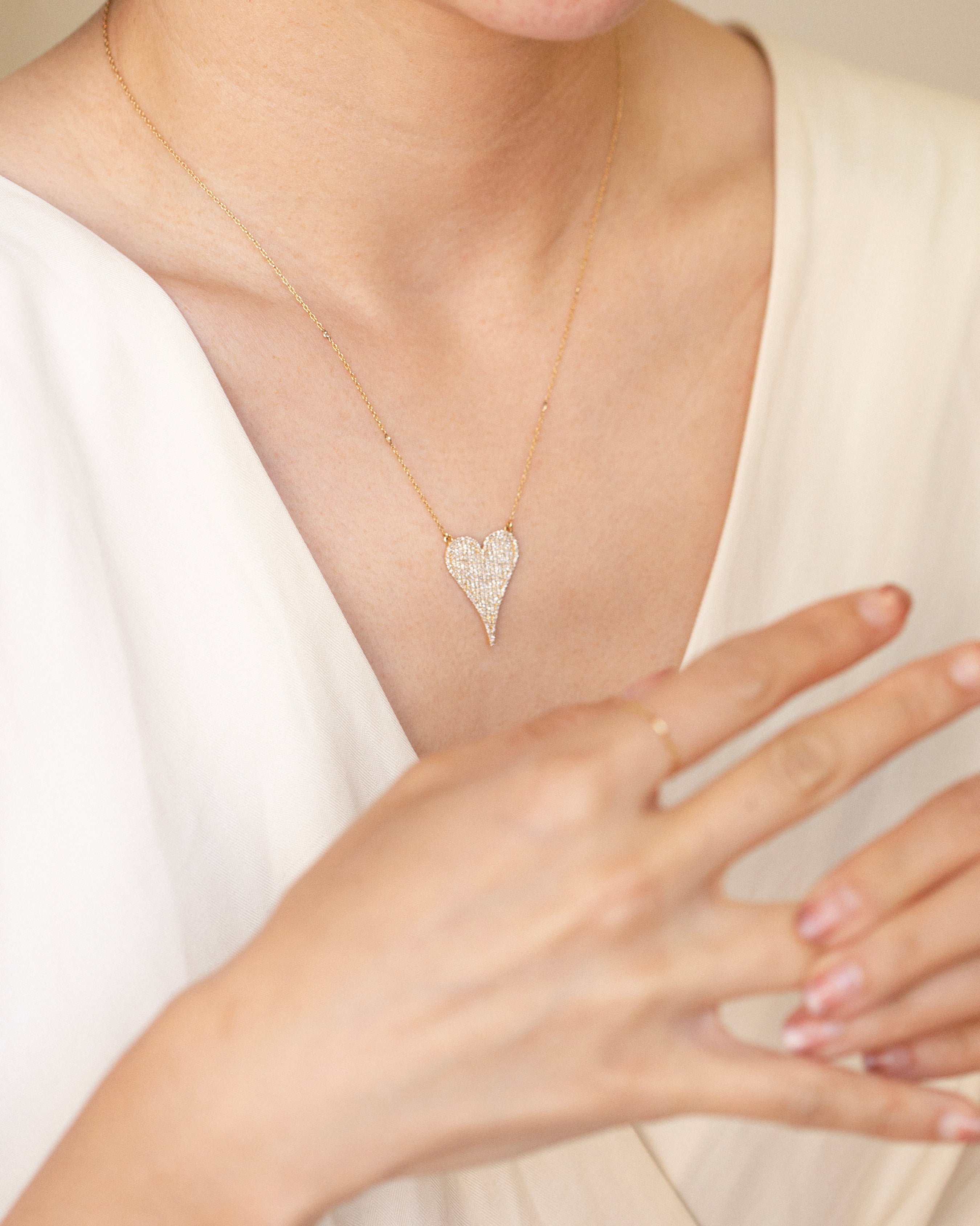 Heart-shaped diamond necklace worn by a person in a white dress.