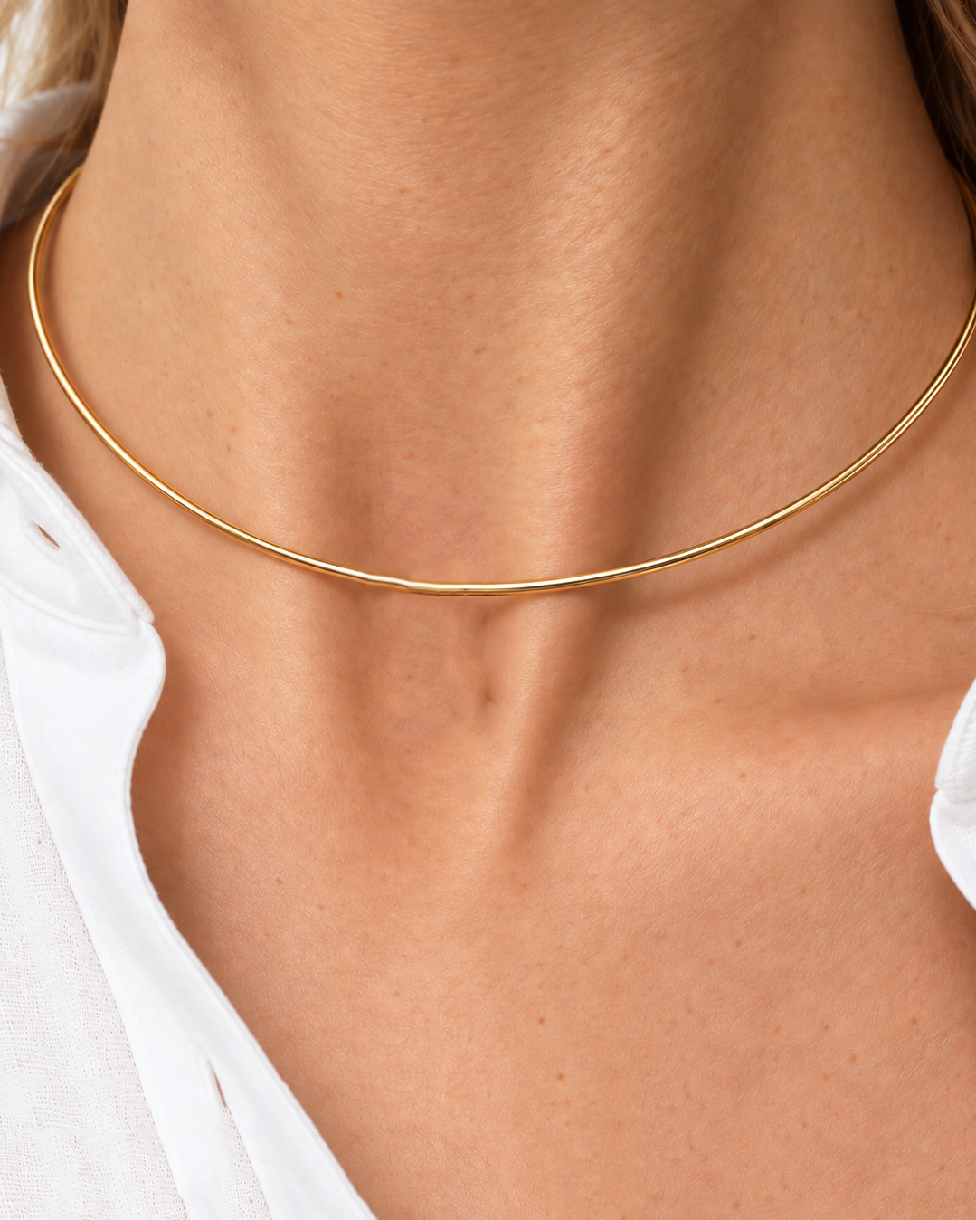 A close-up of a model's neck and collarbone wearing a very thin, delicate gold chain necklace.