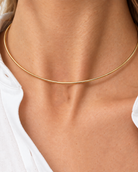 A close-up of a model's neck and collarbone wearing a very thin, delicate gold chain necklace.