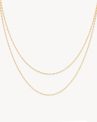 A delicate double-layered gold chain necklace displayed against a clean, off-white background.