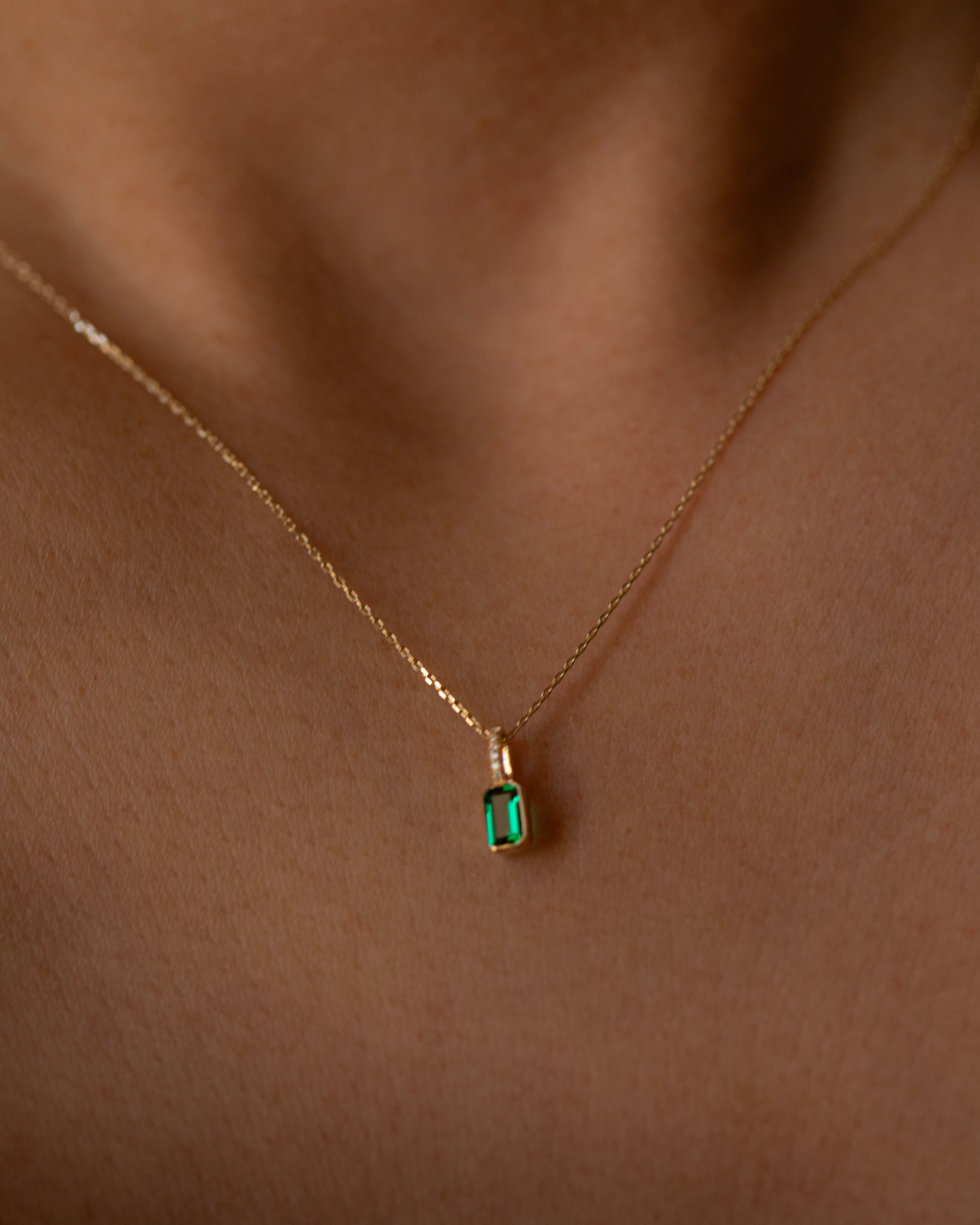 Gold necklace with a green gemstone pendant on a person's neck