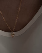 Gold necklace with a heart-shaped pendant on a plain background