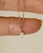 Gold necklace with a diamond pendant held between fingers on a neutral background