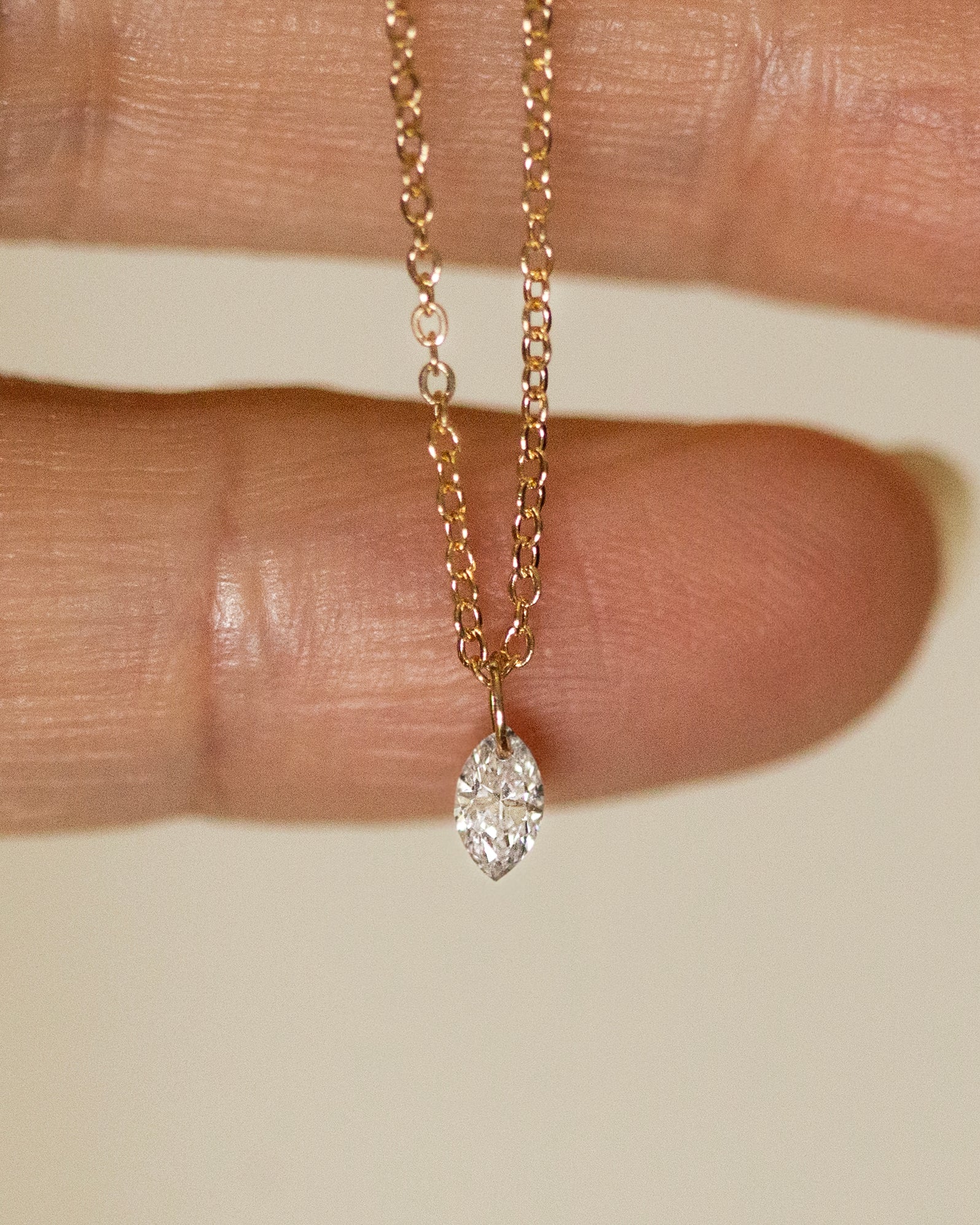 Gold necklace with a diamond pendant held between fingers on a neutral background