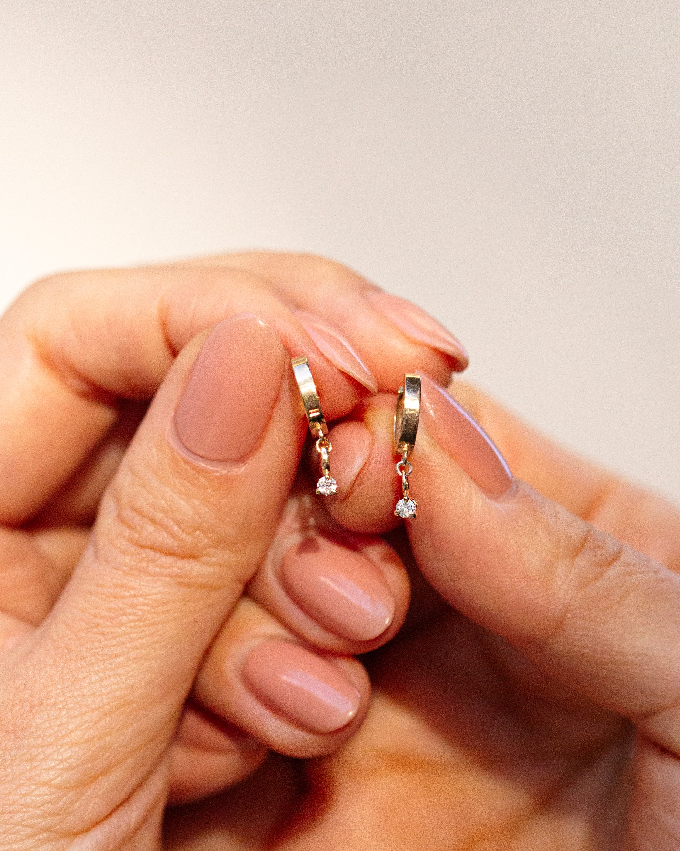 Diamond dangle hoop earrings held by hand.