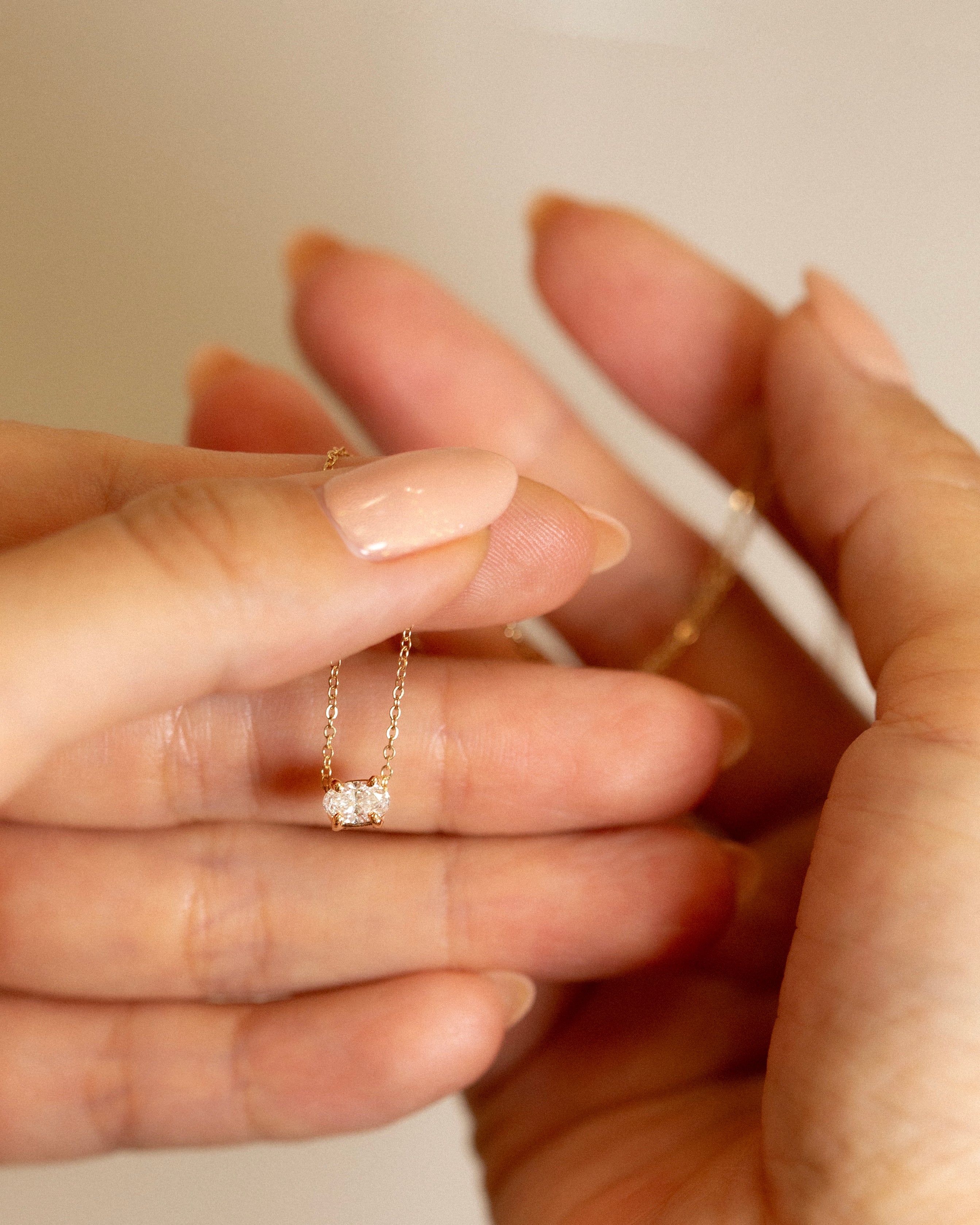 Close-up of a hand wearing a delicate gold ring with a small diamond on a neutral background