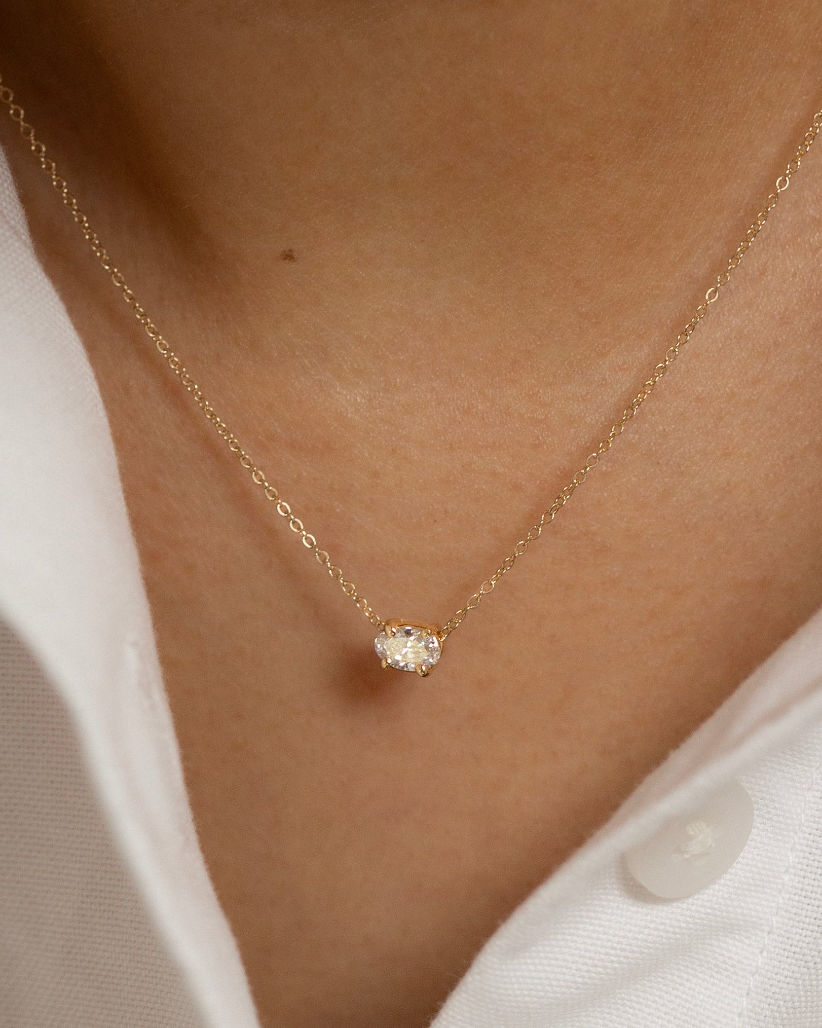 Gold necklace with a small diamond pendant on a person wearing a white shirt.
