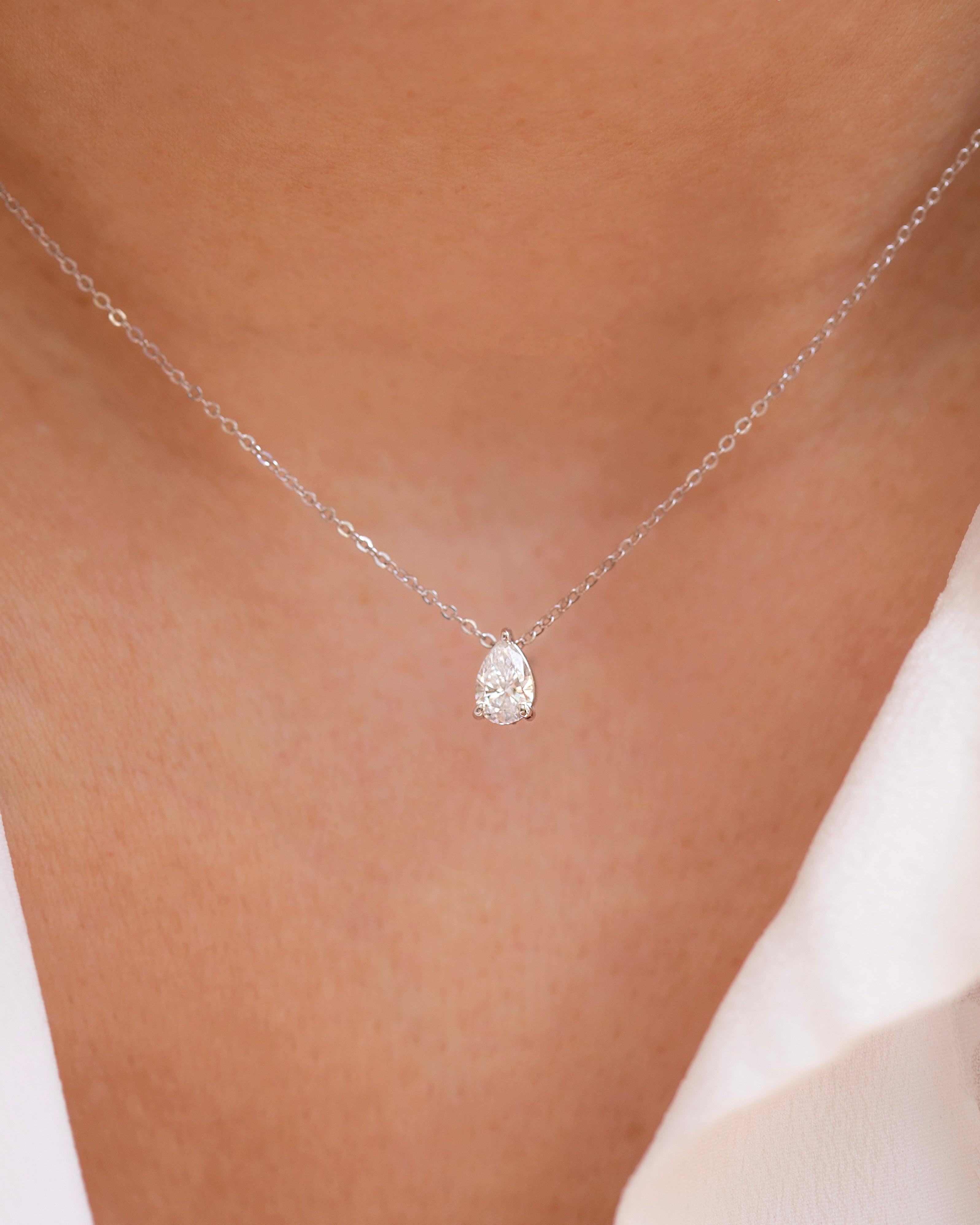 A close-up image of a woman's neck wearing a pear cut diamond solitaire necklace set in a 3-prong setting on a gold chain.