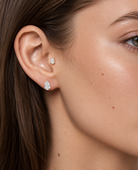 Close-up of a woman's ear wearing two small pear-shaped stud earrings with clear sparkling stones.