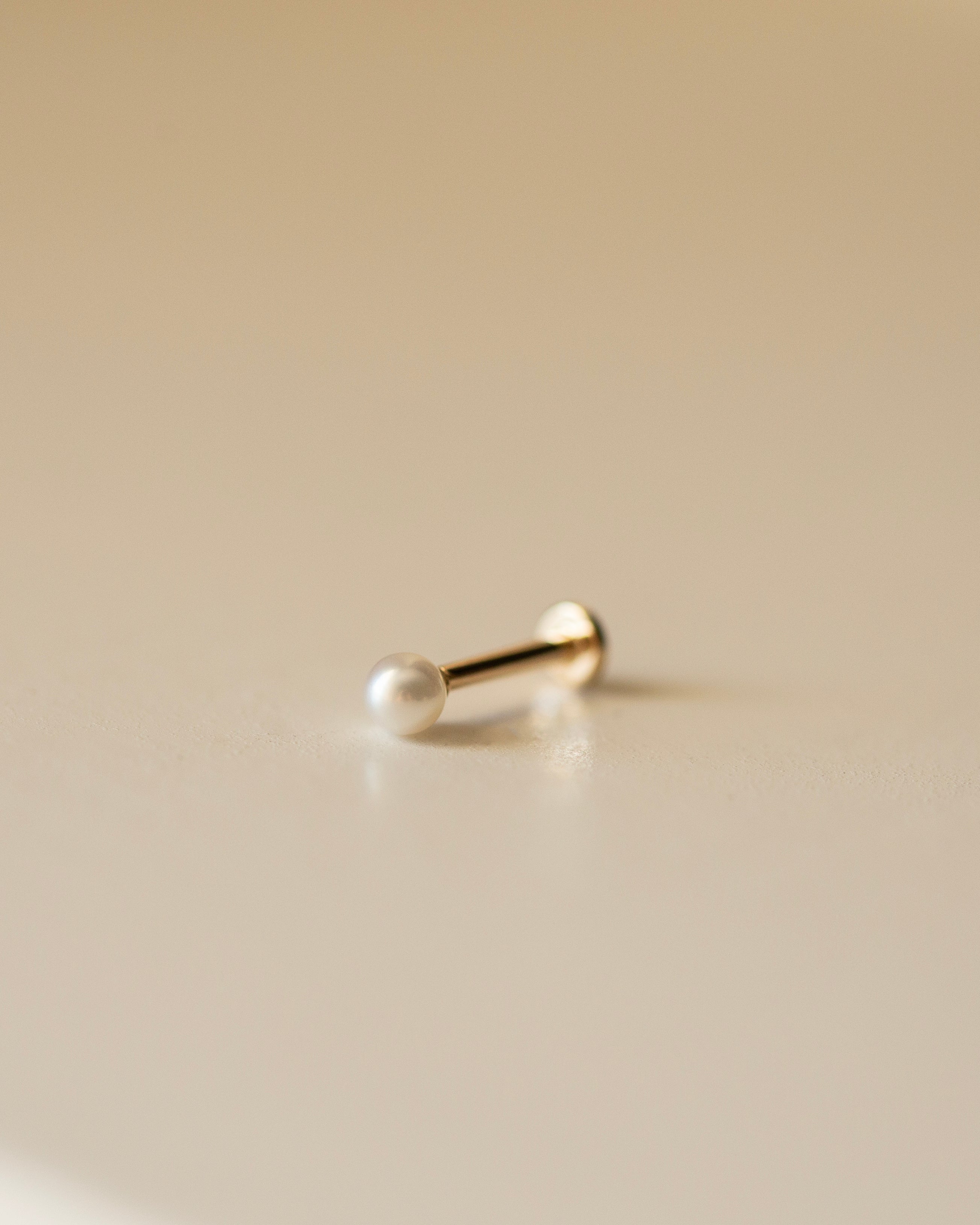 Gold pearl earring on a beige background