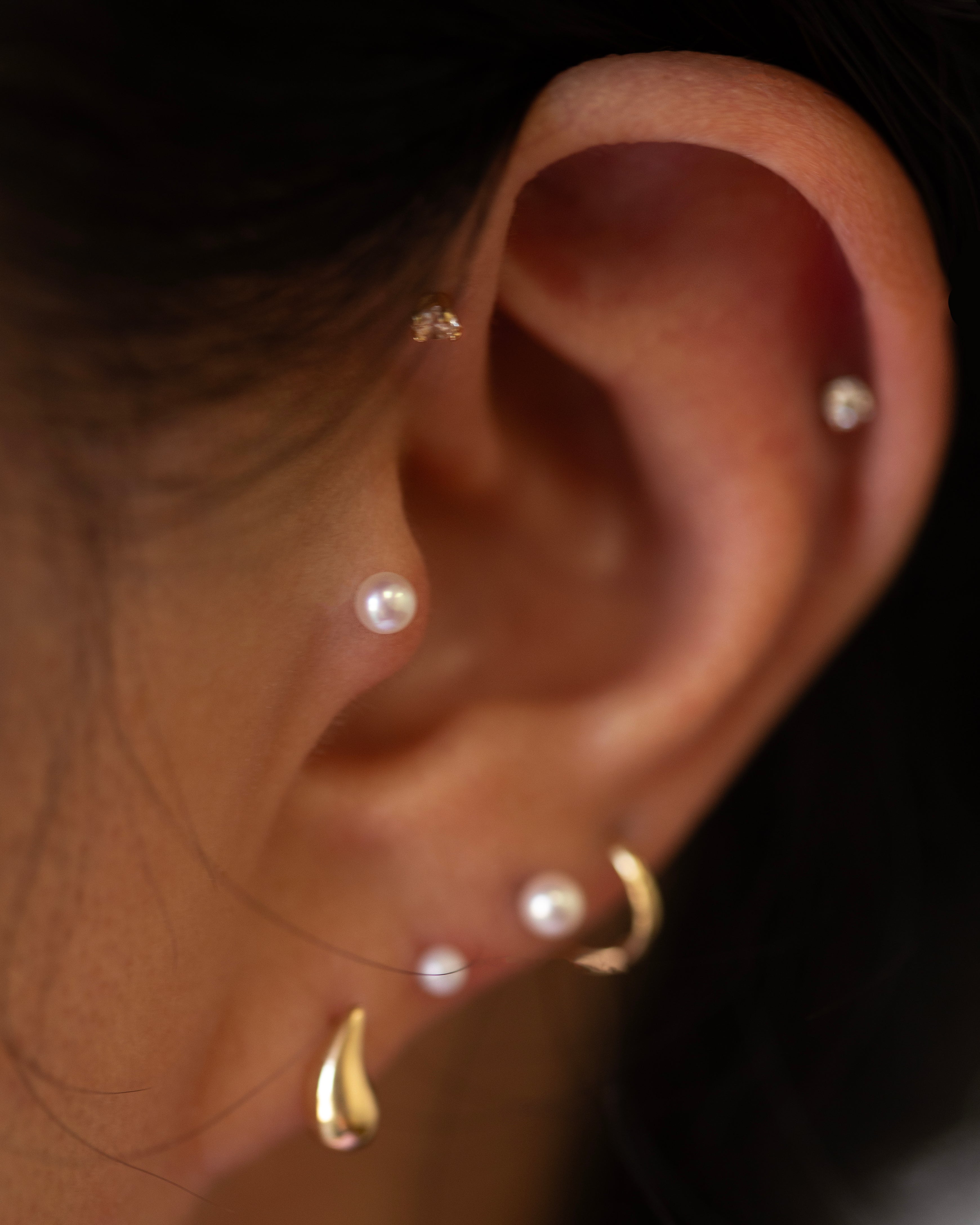 Close-up of an ear with multiple pearl earrings on a dark background