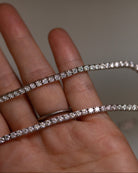 A close-up of a hand holding a delicate white gold tennis bracelet with brilliant diamonds, with a matching silver band visible on the ring finger.