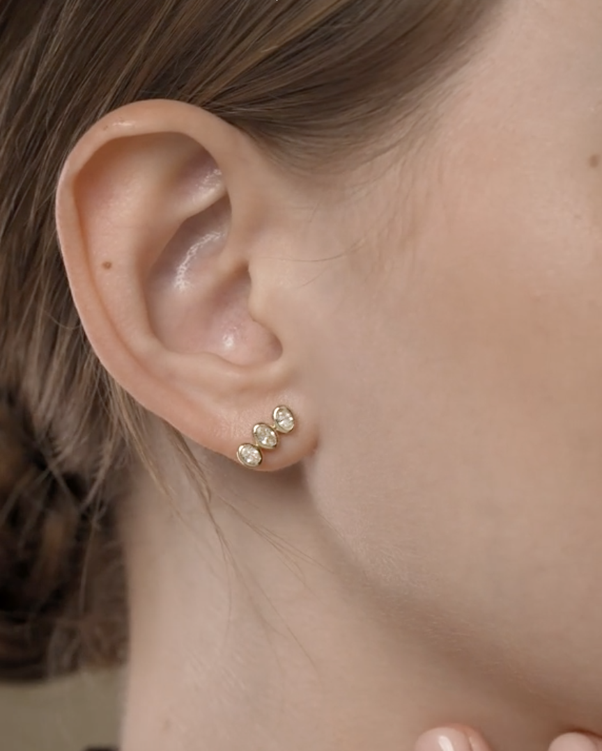Close-up of an ear wearing gold stud earrings with a blurred background