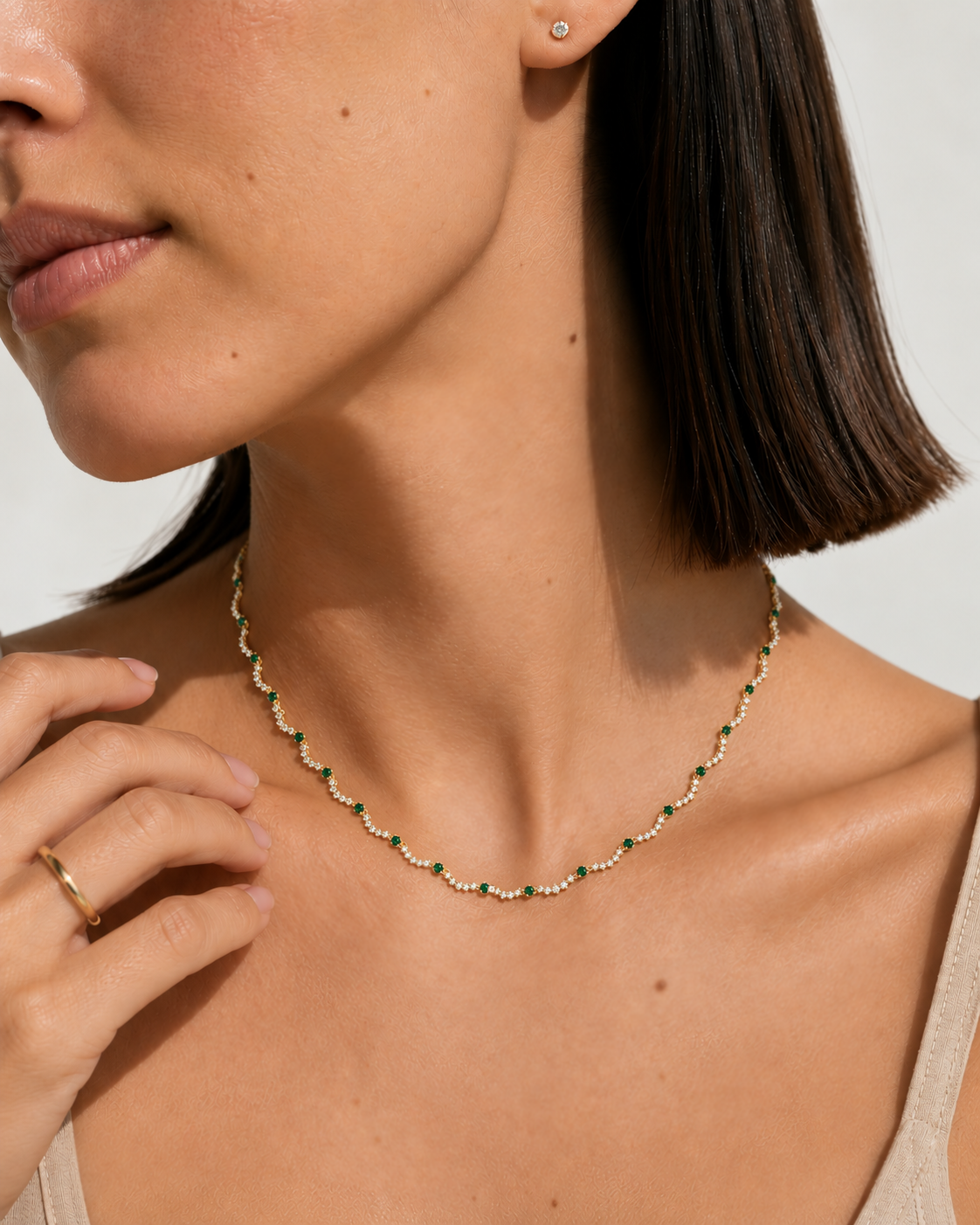 A close-up lifestyle shot of a model wearing a delicate gold chain necklace adorned with small green and white beads, paired with a matching gold ring.