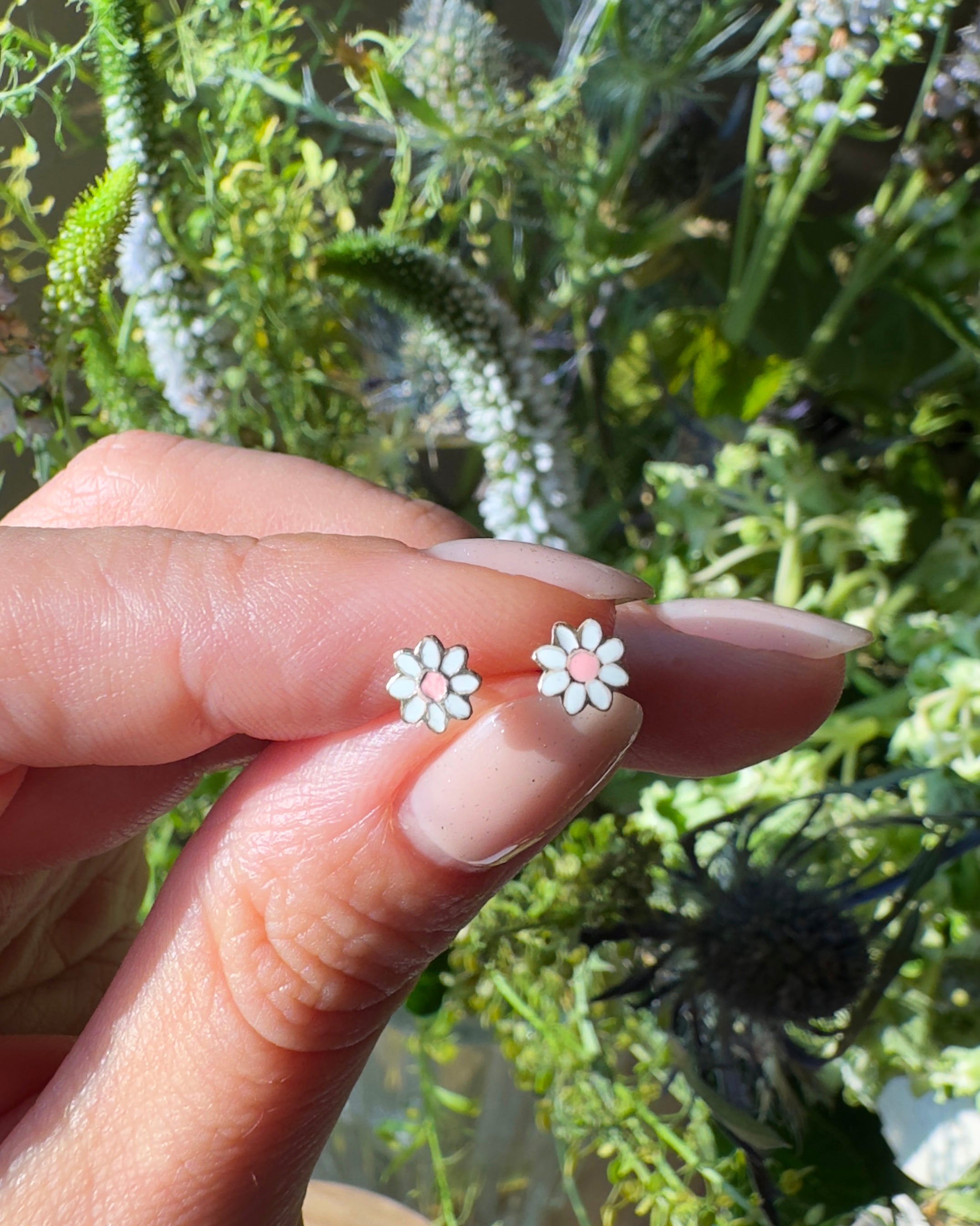 Flower-shaped earrings held between fingers with a natural background